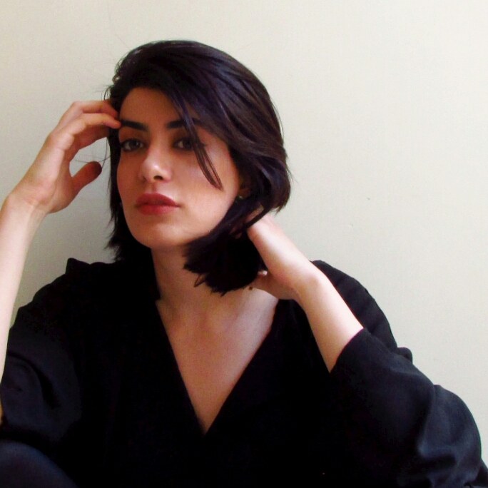 Photo of Maryam: a dark bob, one hand in her hair, the other at her neck, in a black top.